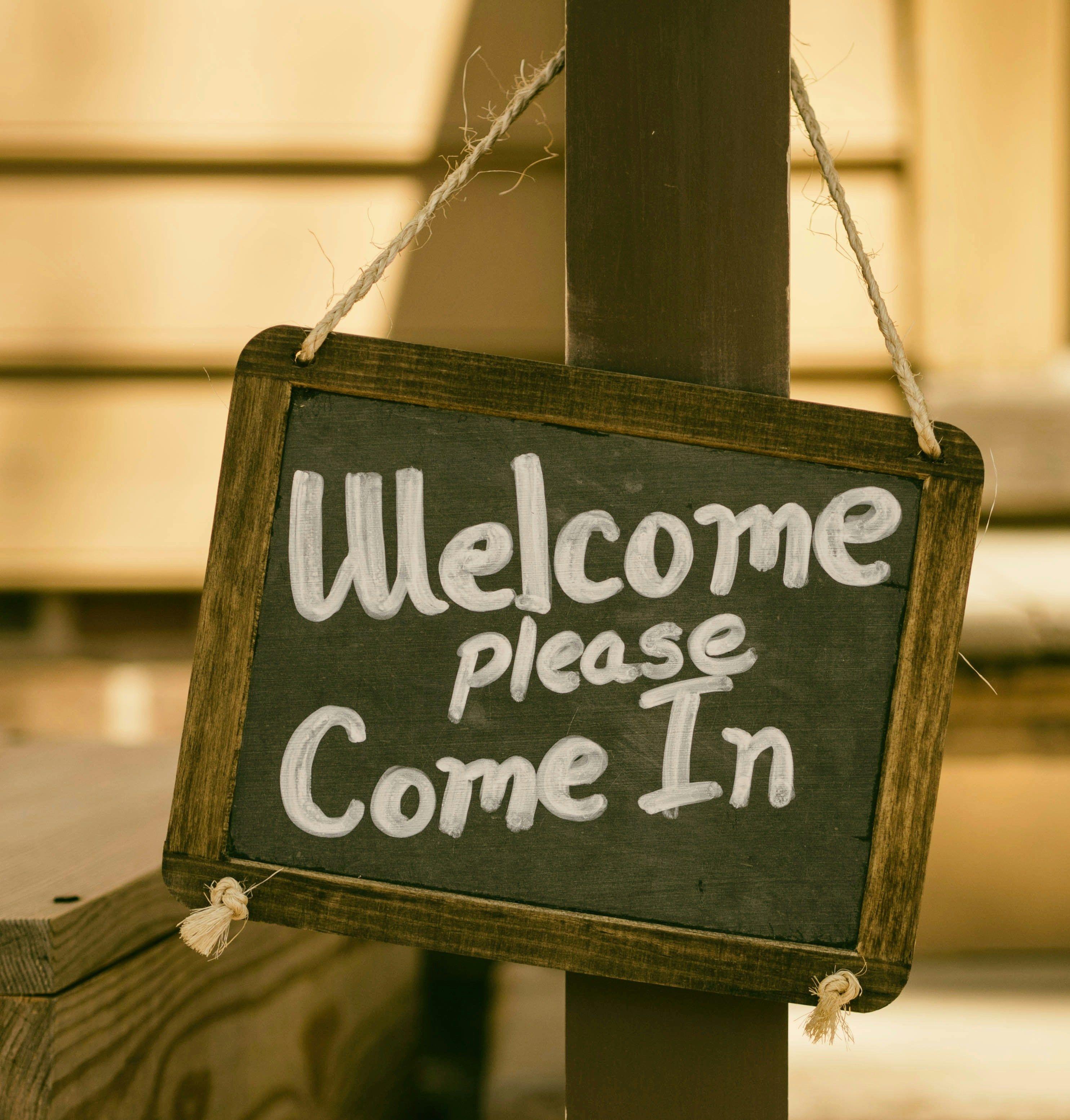 welcome sign hanging on a wooden post